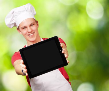 Portrait of young cook man showing a digital tablet against a na