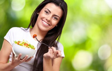 Portrait of healthy woman eating salad against a nature backgrou