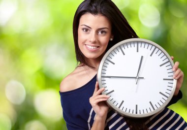Portrait of young woman holding clock against a nature backgroun clipart