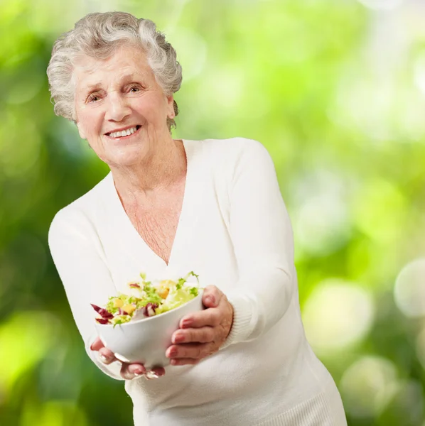 Portrét starší ženy ukazující čerstvý salát proti povahy — Stock fotografie