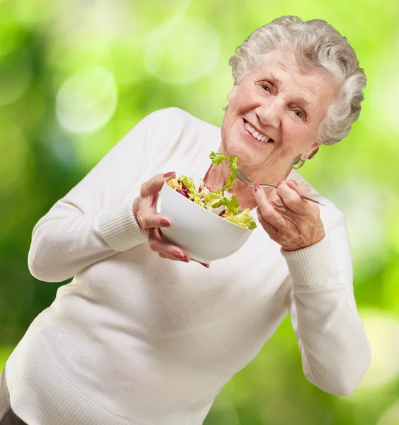 Retrato de una mujer mayor comiendo una ensalada fresca contra una naturaleza b — Foto de Stock