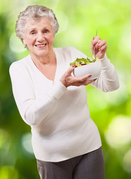 Retrato de mulher sênior comendo salada contra um backgroun de natureza — Fotografia de Stock
