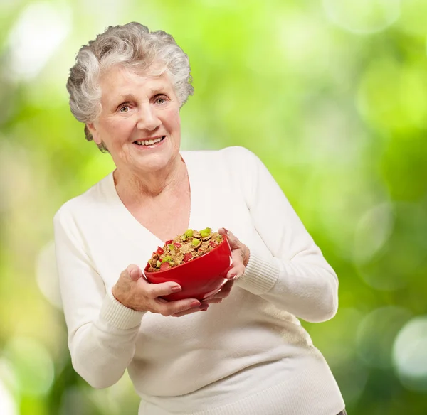 Portrait of healthy senior woman holding cereals bowl against a — Stock Photo, Image