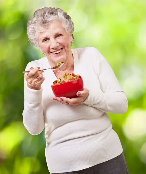 Retrato de una mujer mayor sosteniendo un tazón de cereales contra una naturaleza — Foto de Stock