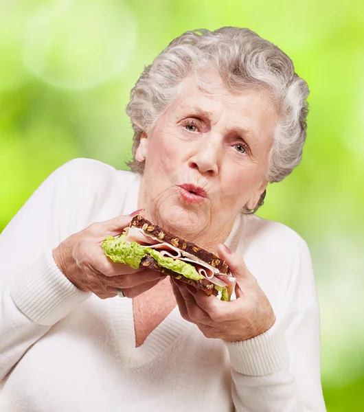 握着美味的三明治针对高级女人肖像 — 图库照片