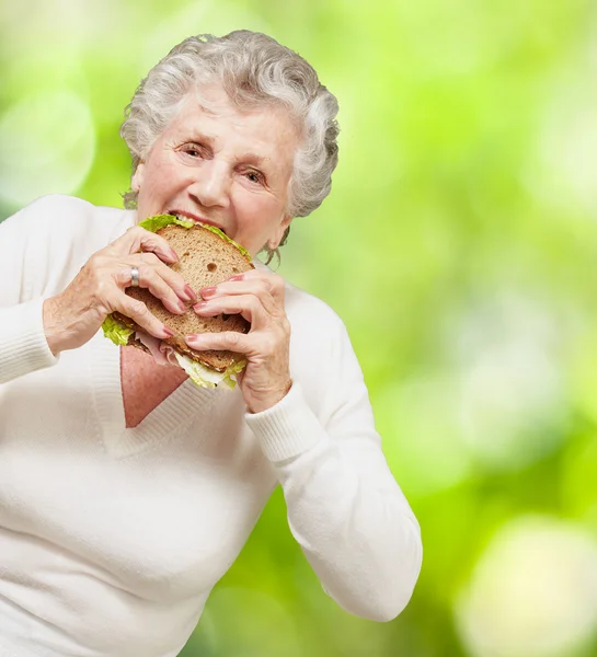 Портрет старшої жінки, що їсть вегетаріанський бутерброд проти природи — стокове фото