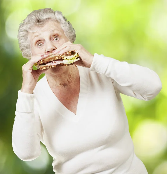 年配の女性が自然れたらに対して健全なサンドイッチを食べる — ストック写真