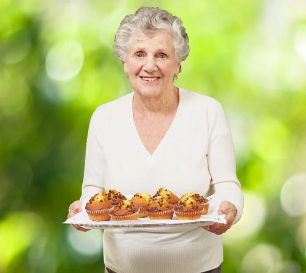 Portrét starší ženy ukazující domácí muffiny proti natu — Stock fotografie