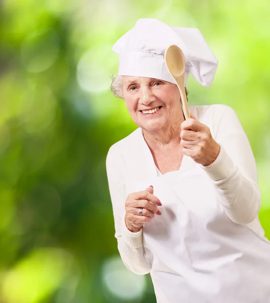 Портрет старшої кулінарної жінки, що тримає дерев'яну ложку на тлі n — стокове фото