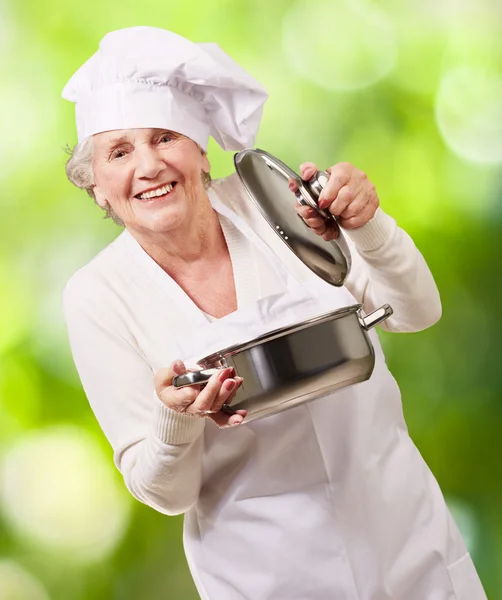 Portret kobiety starszy kucharz, otwarcie sosie patelni wbrew naturze — Zdjęcie stockowe