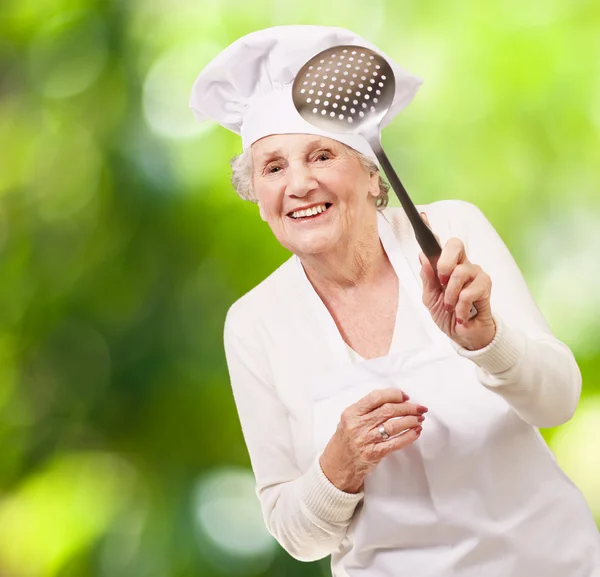 Porträtt av söta senior kock kvinna med en metall sked mot — Stockfoto