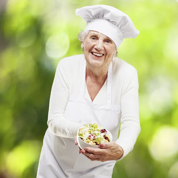 Femme âgée cuisinier tenant un bol avec salade contre un bac nature — Photo