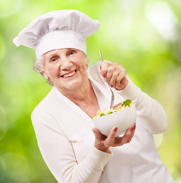 Porträt einer entzückenden Senior-Köchin, die Salat gegen ein na isst — Stockfoto