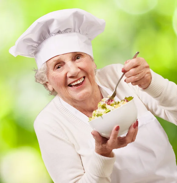 Portrait of senior cook woman eating salad against a nature back — Stock Photo, Image