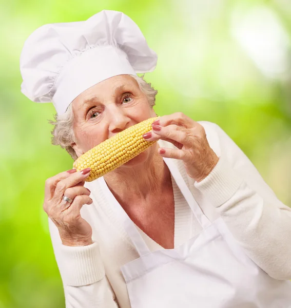 Portrait of senior cook woman eating corn cob against a nature b — Stock Photo, Image