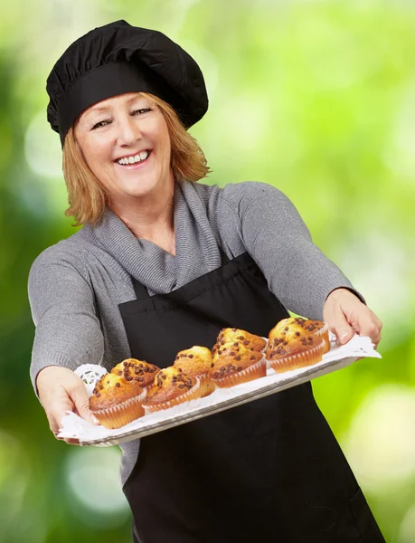 Portrait of cook woman showing a homemade muffins tray against a — Stock Photo, Image