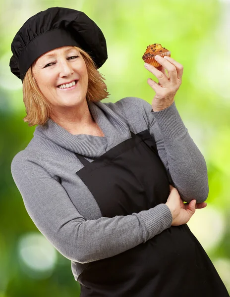 Portrait of middle aged cook woman holding a homemade muffin aga — Stock Photo, Image