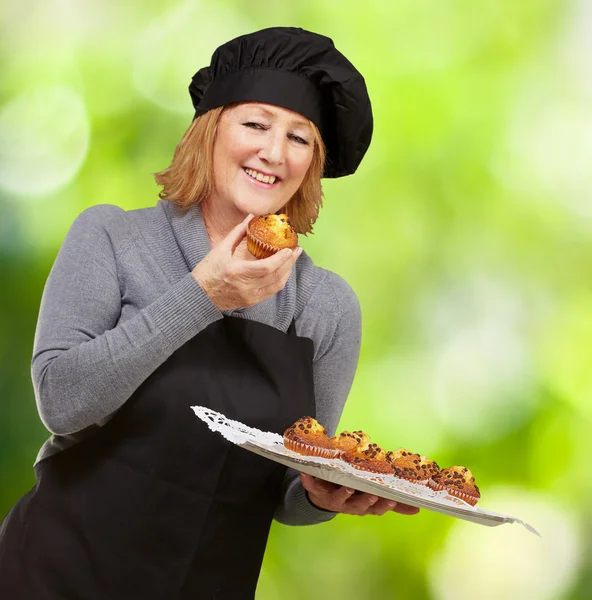 Retrato de meia-idade cozinheiro mulher segurando um muffin caseiro aga — Fotografia de Stock