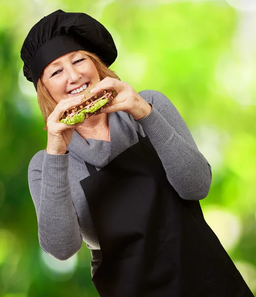 Mulher cozinheira de meia idade segurando um sanduíche vegetal contra um natu — Fotografia de Stock