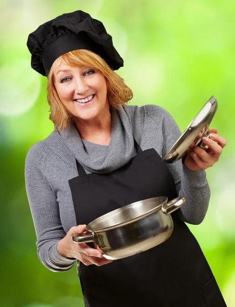 Middle aged cook woman holding a souce pan against a nature back — Stock Photo, Image