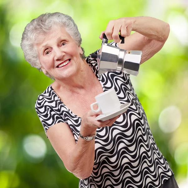 Portrait of a vitality senior woman serving a tea cup against a — Stock Photo, Image