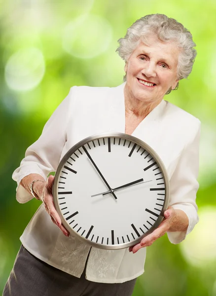 Porträt einer glücklichen Seniorin, die eine Uhr gegen die Natur hält — Stockfoto