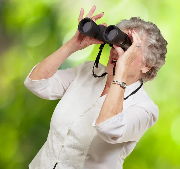 Retrato de una mujer mayor mirando a través de un prismáticos contra un — Foto de Stock