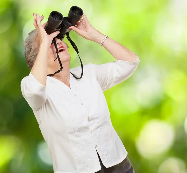 Portrait of senior woman looking through a binoculars against a — Stock Photo, Image