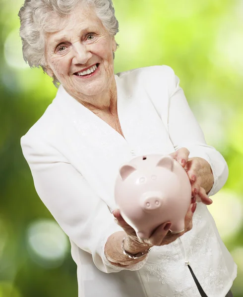 Portrait of senior woman showing a piggy bank against a nature b — Stock Photo, Image