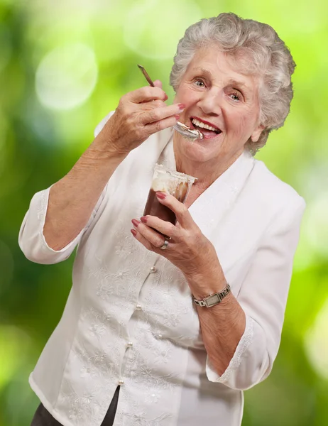 Portret senior kobiety jedzenie czekolady i krem Pucharu przeciwko — Zdjęcie stockowe