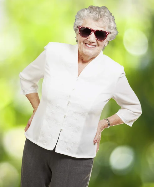 Portrait of senior woman standing wearing sunglasses against a n — Stock Photo, Image