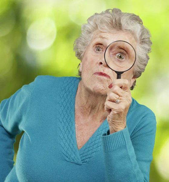 Portrait of senior woman looking through a magnifying glass agai — Stock Photo, Image