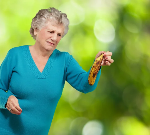 Donna anziana che tiene una banana marcia su uno sfondo naturale — Foto Stock