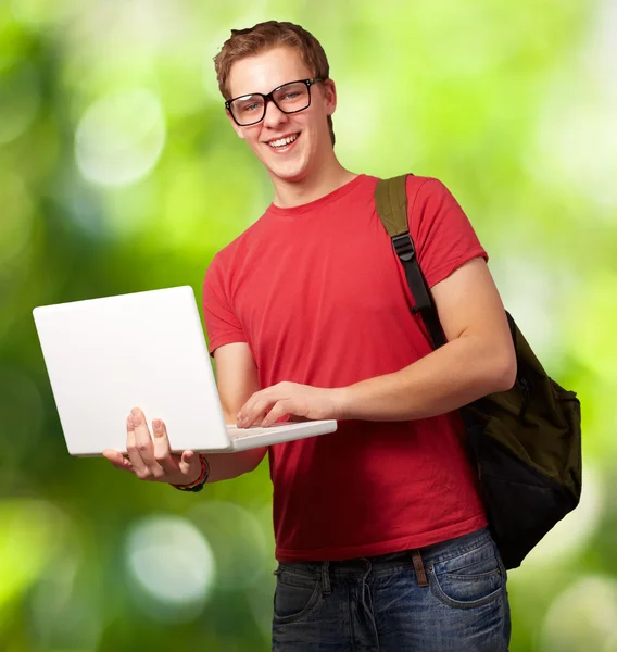 Portrait of young man holding laptop and wearing backpack agains — Stock Photo, Image