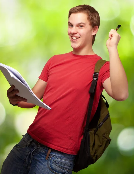 Retrato de un estudiante guapo sosteniendo un cuaderno y una pluma contra un —  Fotos de Stock