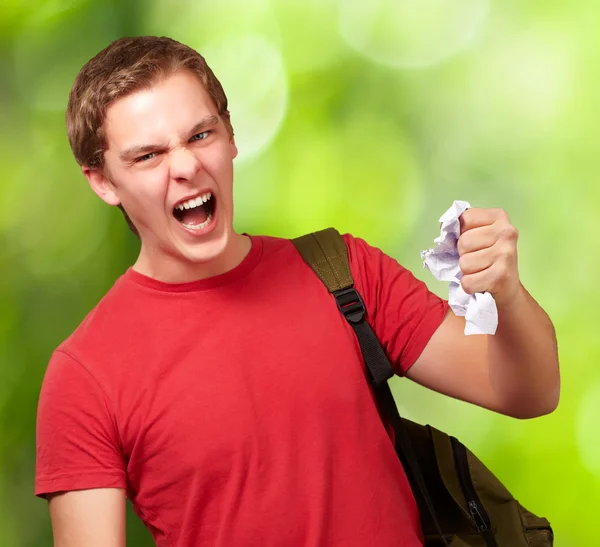 Joven estudiante enojado golpeando una sábana contra una naturaleza backgr — Foto de Stock