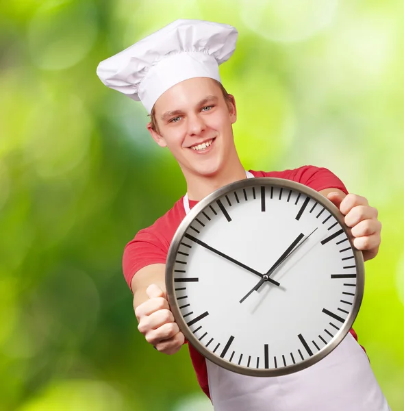 Portrait of young cook man holding clock against a nature backgr — Stock Photo, Image