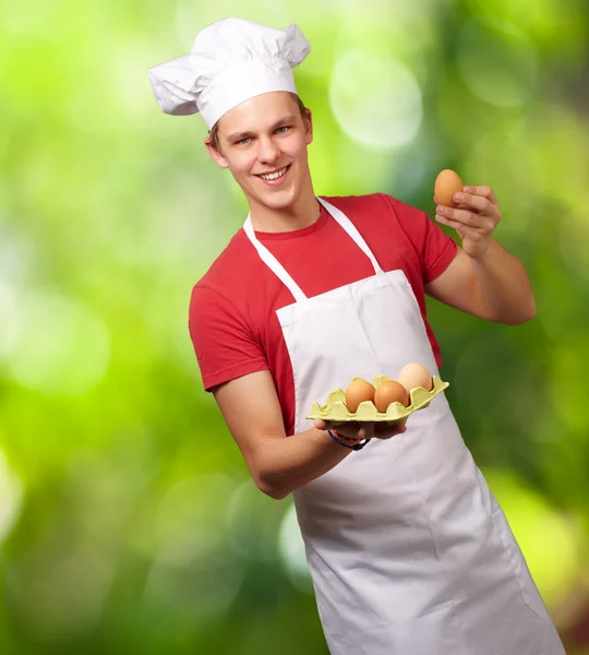 Portrait of young cook man holding egg box against a nature back — Stock Photo, Image