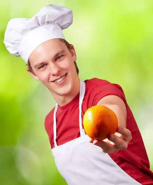 Retrato del joven cocinero ofreciendo naranja contra la naturaleza backgr — Foto de Stock