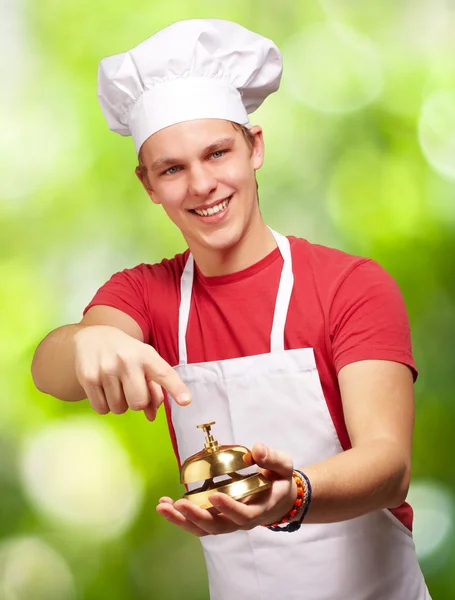 Retrato del joven cocinero presionando una campana dorada contra un natu — Foto de Stock