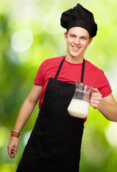 Portrait of young cook man holding milk jar against a nature bac