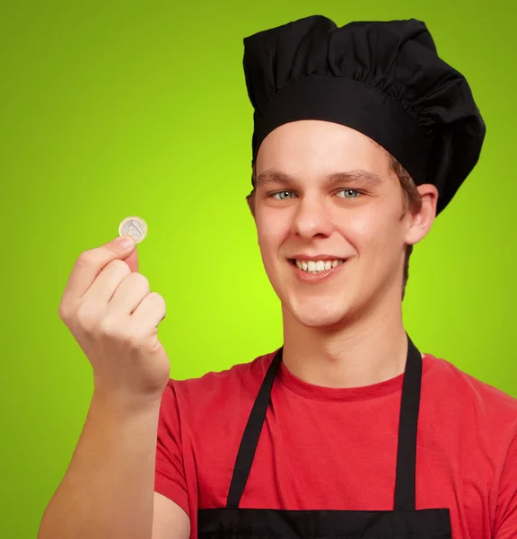 Portrait d'un jeune cuisinier tenant une pièce en euros et une tirelire — Photo