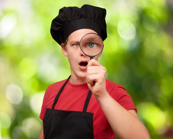 Portrait of young cook man looking through a magnifying glass ag — Stock Photo, Image