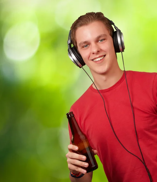 Retrato de jovem ouvindo música e segurando cerveja contra um — Fotografia de Stock