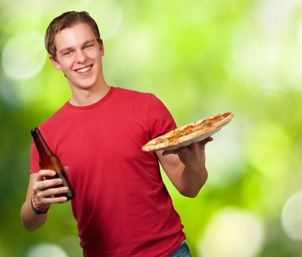 Portrait of young man holding pizza and beer against a nature ba — Stock Photo, Image