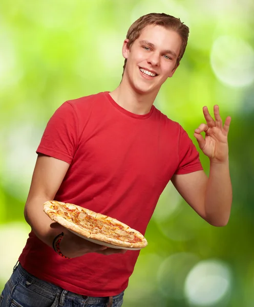 Retrato do jovem segurando pizza e fazendo bom gesto novamente — Fotografia de Stock