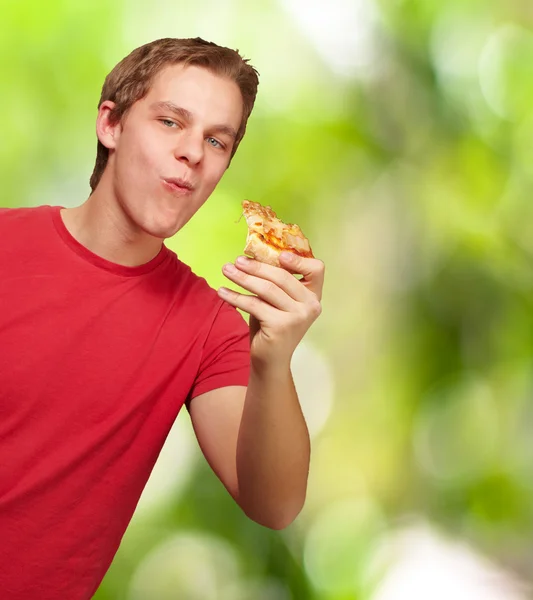 Portrait of young man eating pizza portion against a nature back — Stock Photo, Image