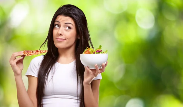 Portret van een jonge vrouw pizza of salade tegen een karakter kiezen — Stockfoto