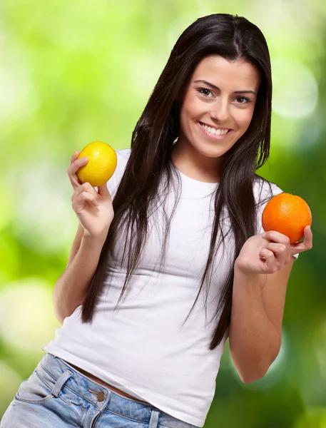 Joven chica bonita sosteniendo naranja y limón contra una naturaleza espalda — Foto de Stock