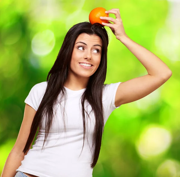 Retrato de mujer joven sosteniendo naranja en su cabeza sobre la naturaleza b —  Fotos de Stock